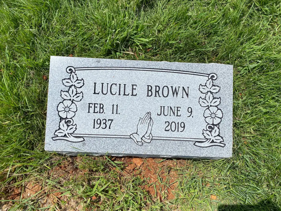 A grey granite flat marker set in the grass, with flowers carved in the corners