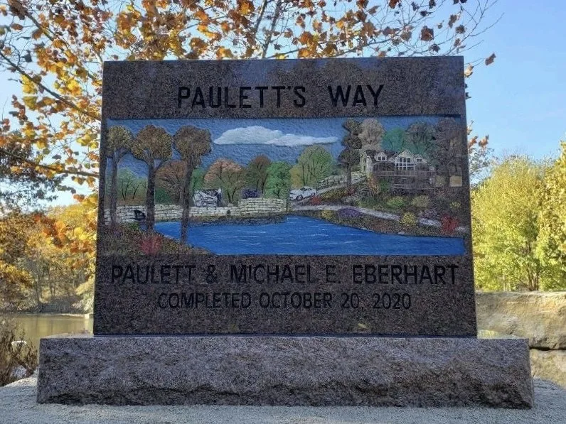 Paulett's Way, a granite monument with a lake, trees and a house painted in full color, set among autumn trees