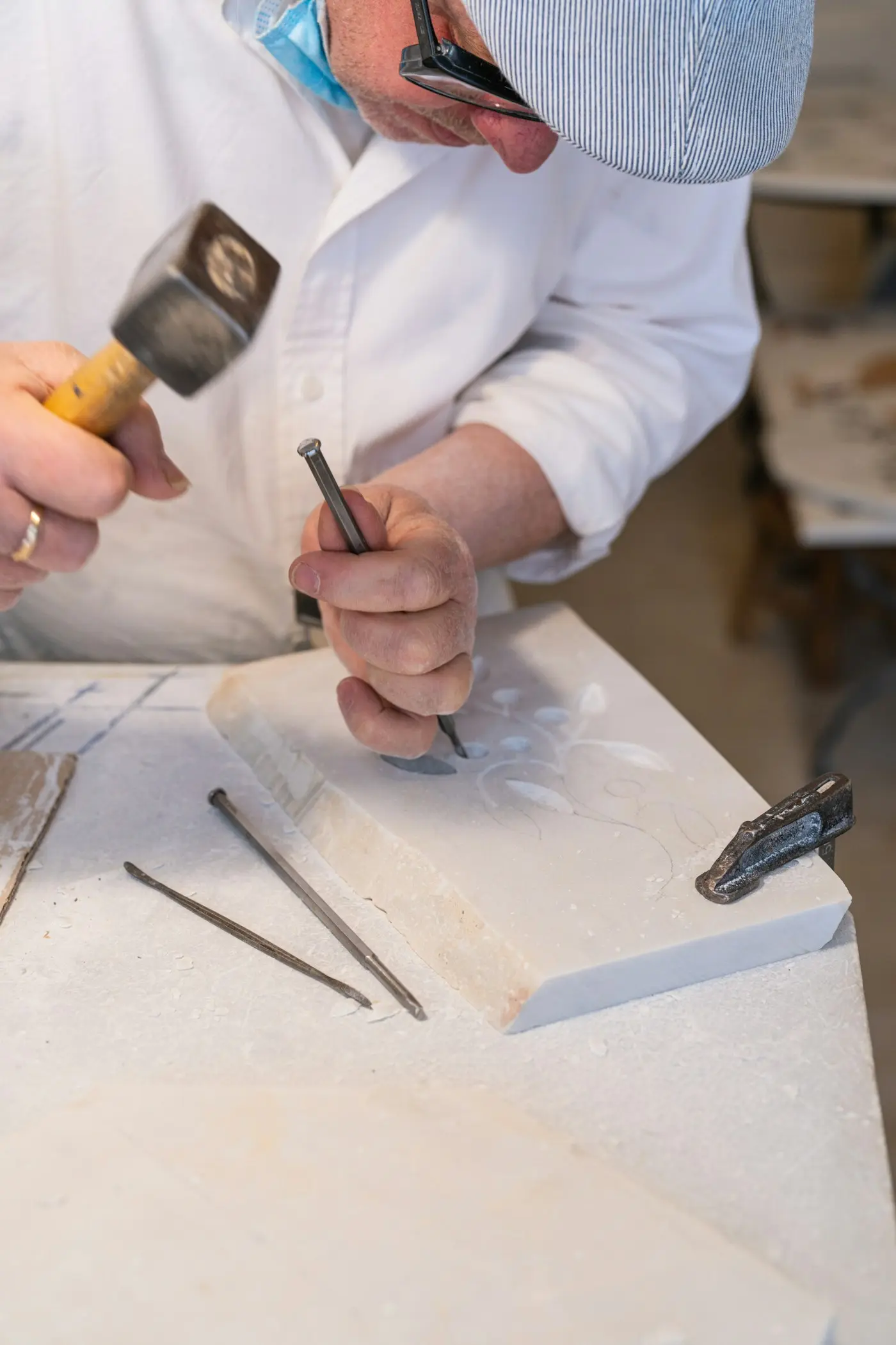 A carver cutting an ornament into stone with a mallet and chisel